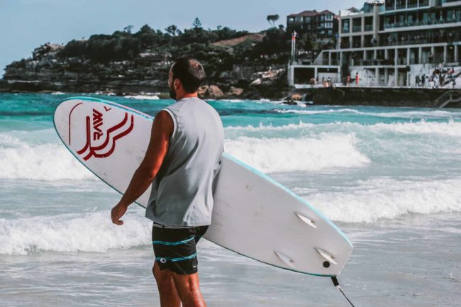 pexels-photo-785133 man walking towards body of water holding a surfboard